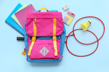 Badminton raketleri, servis aleti ve mavi arka planda farklı kırtasiye malzemeleri.