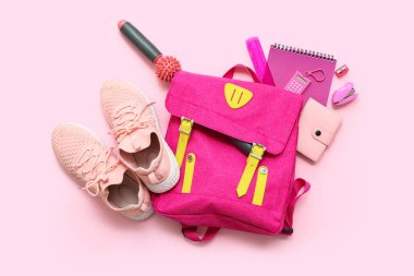 Spor ayakkabılar, masaj çubuğu ve pembe arka planda farklı kırtasiye malzemeleri.
