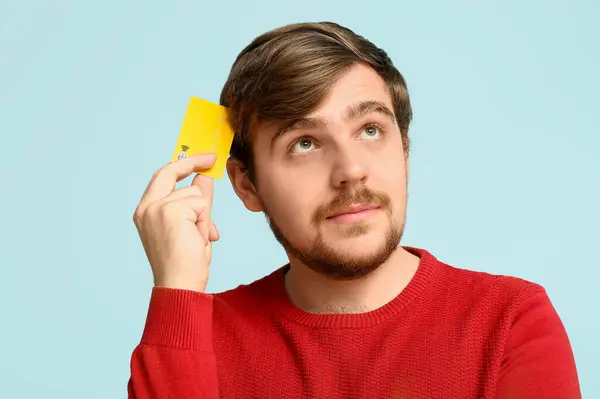 Stock image Thoughtful young man with credit card on blue background