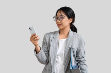 Gri arka planda klasörü ve cep telefonu olan mutlu Asyalı genç iş kadını