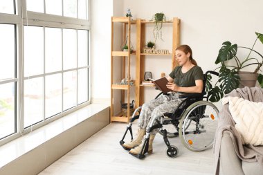 Tekerlekli sandalyedeki kadın asker evde kitap okuyor.