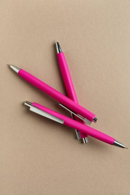 Bej arka planda üç pembe kalem. Üst görünüm