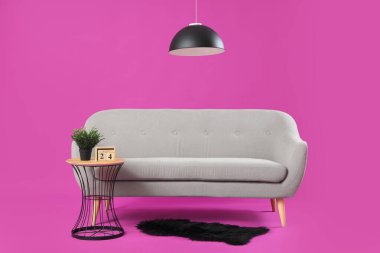 Modern oturma odasının içinde gri kanepe, masa ve lamba pembe arka planda.