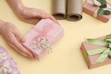 Hediye kutuları, ambalaj kağıtları ve sarı arka planda çiçekler olan kadın elleri. Uluslararası Kadınlar Günü