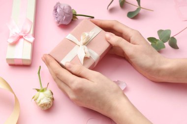Hediye kutularıyla kadın elleri ve pembe arka planda güzel güller. Uluslararası Kadınlar Günü
