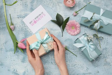 Hediye kutuları, kart ve mavi arka planda güzel çiçekler olan kadın elleri. Uluslararası Kadınlar Günü