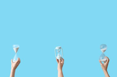 Mavi arka planda kum saati tutan kadın eller.