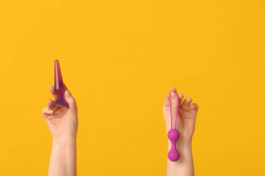 Sarı arka planda anal tıkaç ve vajinal toplara sahip kadın elleri, yakın plan.