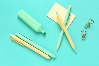 İşaretli kalemler, yapışkan notlar ve turkuaz arkaplan üzerindeki cilt klipleri