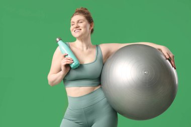 Spor topu ve yeşil arka planda bir şişe suyu olan genç bir kadın.