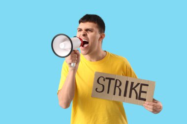 Protesto eden genç adam megafona bağırıyor ve mavi arka planda kelime STRIKE ile pankart tutuyor