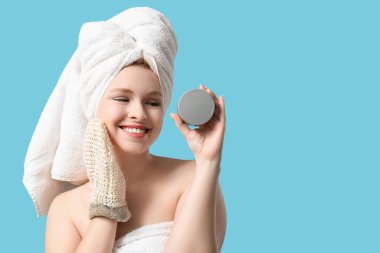 Güzel, genç, mutlu bir kadın. Masaj eldiveni ve mavi arka planda bir kavanoz krema.