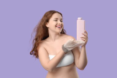 Banyo masaj eldiveni ve mor arka planda bir şişe duş jeli olan genç ve güzel bir kadın.