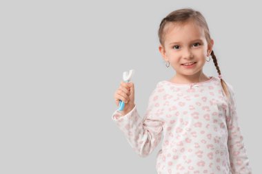 Gri arka planda diş fırçası olan mutlu küçük kız.