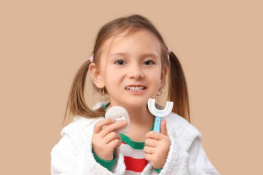 Kahverengi arka planda diş fırçası ve diş ipi olan bornozlu mutlu küçük kız.