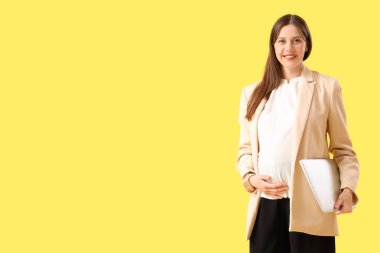 Sarı arka planda dizüstü bilgisayarı olan hamile bir iş kadını.