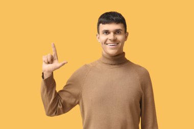 Sarı arka planda işaret dili kullanan genç sağır ve dilsiz adam.