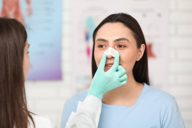 Klinikte burnu bandajlı plastik cerrah ve genç bir kadın.