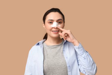 Kahverengi arka plandaki sargılı burnu gösteren genç bir kadın. Estetik ameliyat konsepti