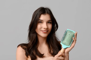 Gri arka planda turkuaz saç fırçası olan güzel bir genç kadın.