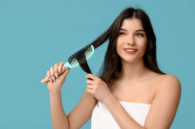 Saçlarını mavi arka planda tarayan güzel genç bir kadın.