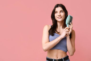 Saçlarını pembe arka planda tarayan güzel bir genç kadın.