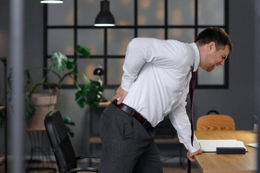 Geceleri ofiste sırt ağrısı çeken genç bir işadamı.