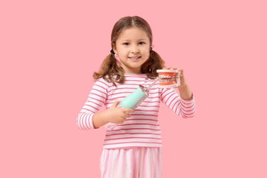 Ağız sulandırıcısı ve pembe arka planda çene modeli olan tatlı küçük kız.