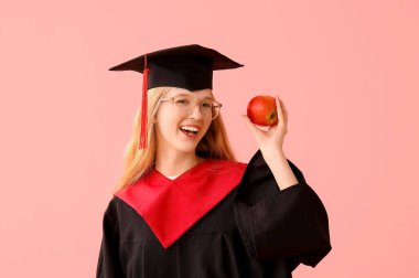 Pembe arka planda elma taşıyan havan tahtasındaki mezun bayan öğrenci.