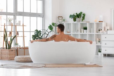 Yakışıklı adam evde köpükle banyo yapıyor.