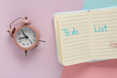 Liste yapmak için metin ve renkli arkaplan üzerinde alarm saati ile defteri aç. Zaman yönetimi konsepti. Üst görünüm