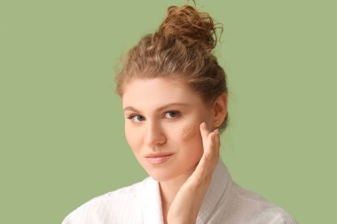 Yüzünde yeşil arka planda makyaj temeli olan güzel bir genç kadın.