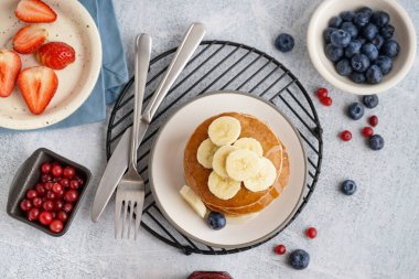 Lezzetli krep, muz dilimleri, yaban mersini ve çatal bıçaklı tabaklar beyaz masaya.