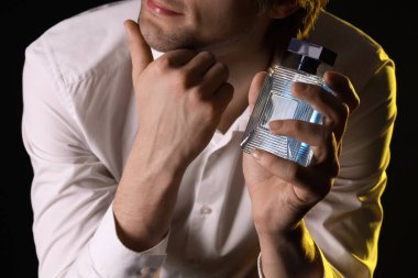 Siyah arka planda parfüm şişesi olan yakışıklı bir adam. Yakın çekim.