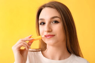 Güzel genç bir kadın sarı arka plana hijyenik dudak kremi sürüyor.