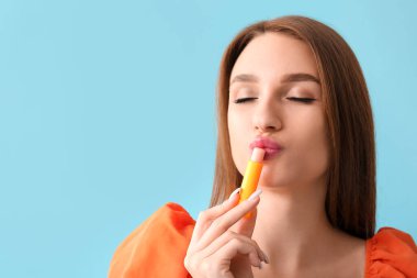 Mavi arka planda dudak kremi olan güzel genç bir kadın.