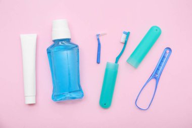 Diş macunlu gargara, diş fırçası ve pembe arka planda dil kazıyıcı.