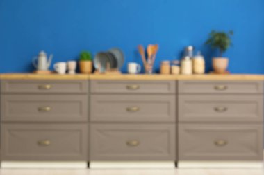 Mavi duvarın yanındaki tezgah ve çatal bıçaklarla modern mutfağın bulanık görüntüsü