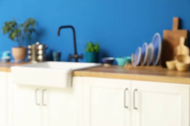 Mavi duvarın yanında tezgah, lavabo ve çatal bıçak ile modern mutfağın bulanık görüntüsü