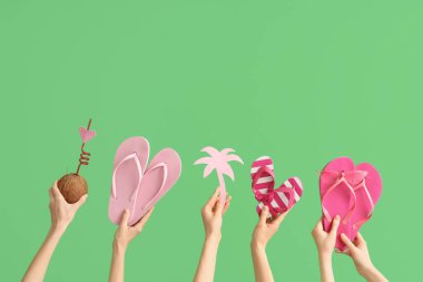 Hindistan cevizi, kağıt avuç içi ve yeşil arka planda güneş gözlüklü üç çift parmak arası terlik tutan eller.