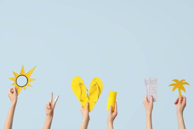 Mavi arka planda parmak arası terlik, bilet ve plaj aksesuarları olan eller.