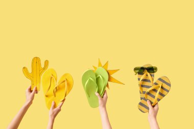 Ellerinde üç çift parmak arası terlik, güneş gözlüğü, kağıt güneş ve sarı arka planda kaktüs vardı.