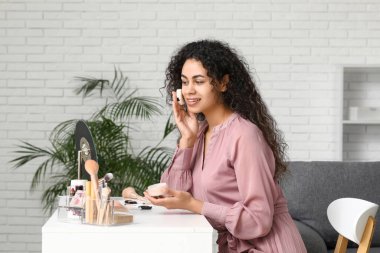 Güzel, mutlu, Afro-Amerikan bir kadın evde makyaj yaparken pudra sürüyor.