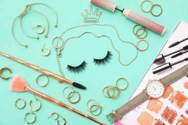 Takma kirpik, kol saati, makyaj aksesuarları ve turkuaz arka planda takılı yaratıcı kompozisyon