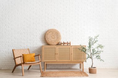 Konforlu koltuğu, zeytin ağacı ve beyaz tuğla duvarın yanındaki çekmeceleri olan aydınlık oturma odasının içi.