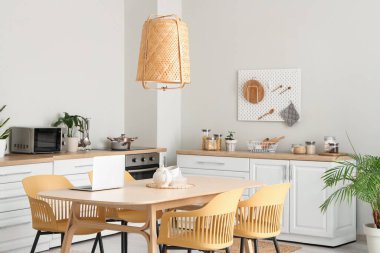 Modern mutfak, beyaz tezgahlar, yemek masası, dizüstü bilgisayar, sandalyeler ve lamba.