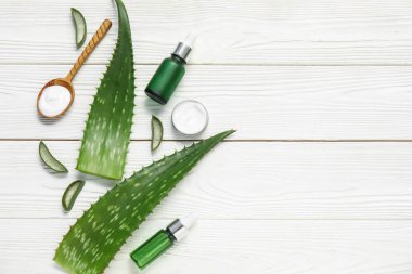 Aloe Vera yaprakları, kavanoz ve beyaz ahşap zemin üzerinde kozmetik ürünler şişeleri
