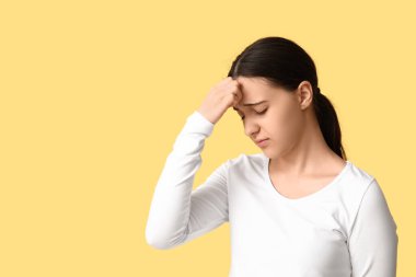 Sarı arka planda baş ağrısı çeken güzel bir genç kadın.