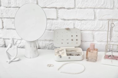 Beyaz tuğla duvarın yanındaki masada ayna ve parfüm şişesi olan farklı mücevherler.