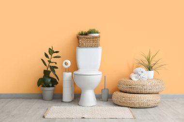 Tuvaletin içinde bej duvarın yanında klozet, puf ve bitkiler var.